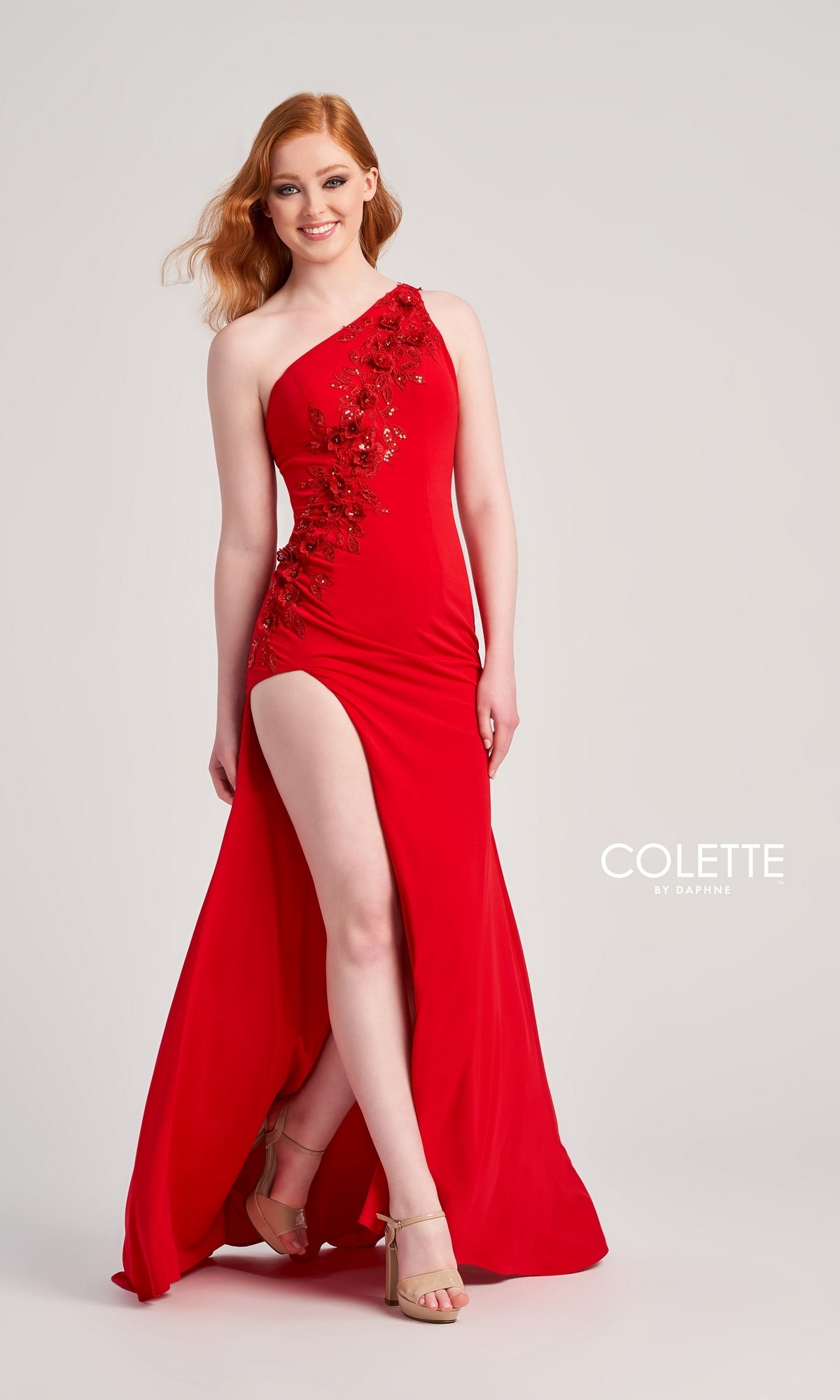 A woman in a red Colette One-Shoulder Sleek Long Prom Dress CL5108 with floral details and a high slit smiles against a plain light background.